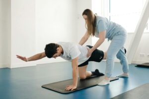 A female exercise physiologist guiding a patient through a leg-raise floor exercise for rehabilitation.