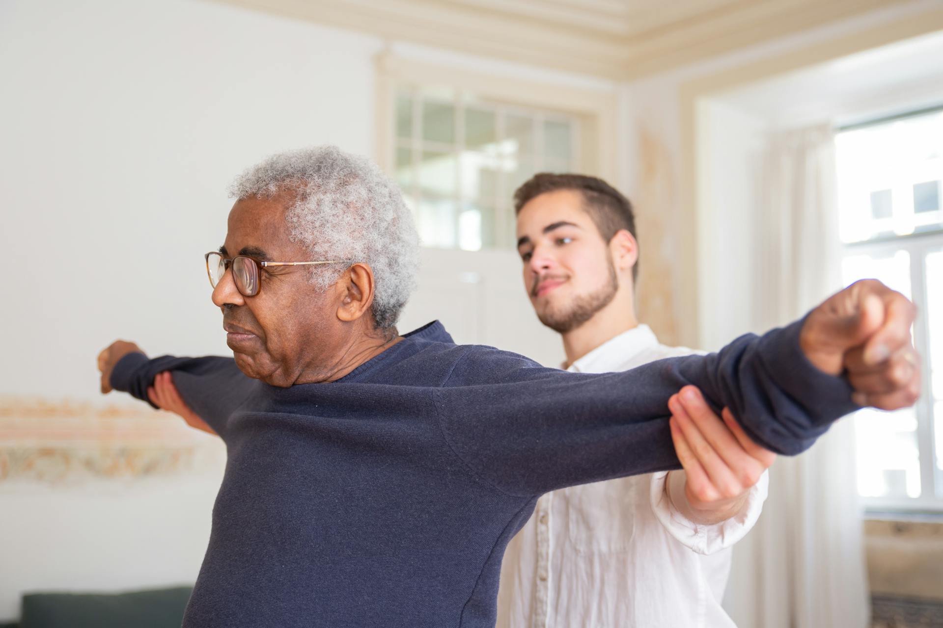 A physiotherapist assisting an elderly patient with strength and flexibility exercises in a clinical setting.